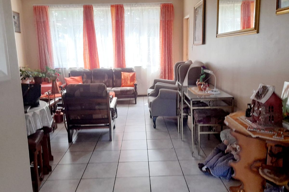 A living room area featuring tiled flooring and large windows with curtains, providing a functional space for relaxation.