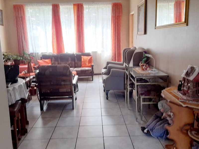 A living room area featuring tiled flooring and large windows with curtains, providing a functional space for relaxation.