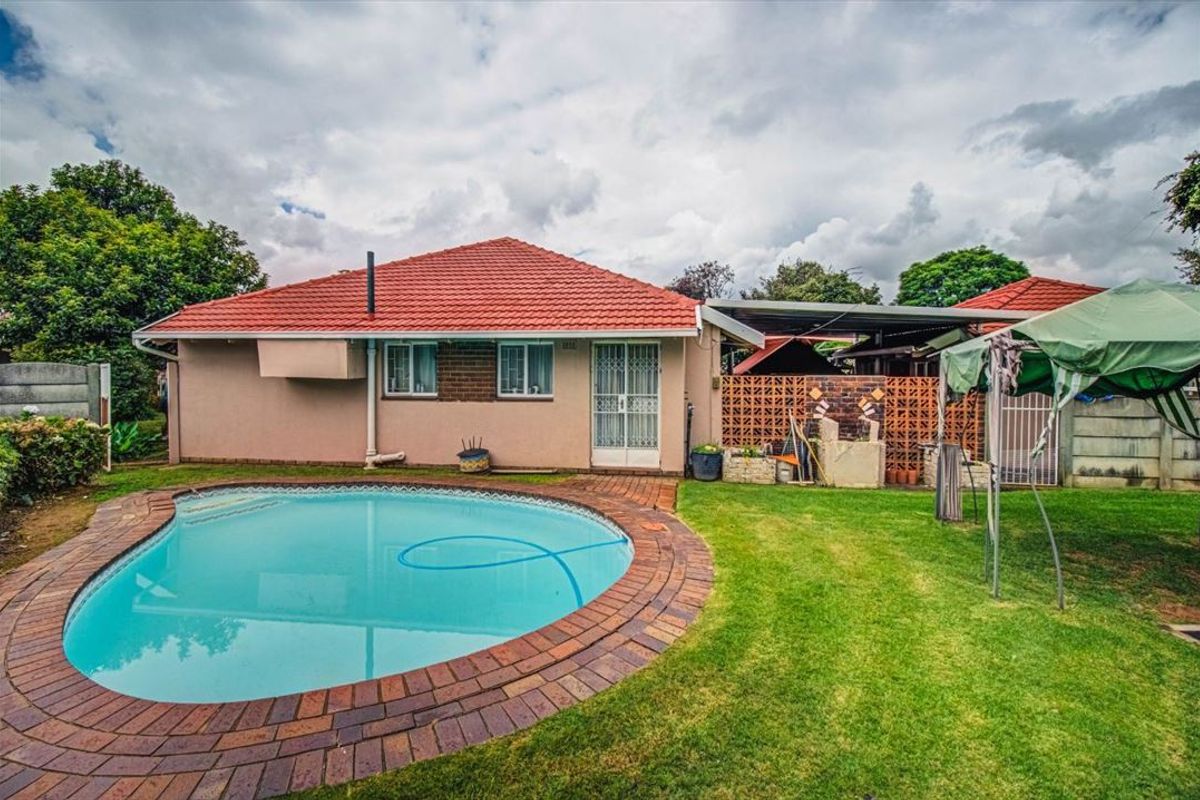 Rear view of the property featuring a swimming pool with brick coping, a covered patio area, and a well-maintained garden.