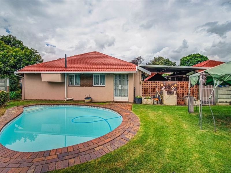 Rear view of the property featuring a swimming pool with brick coping, a covered patio area, and a well-maintained garden.