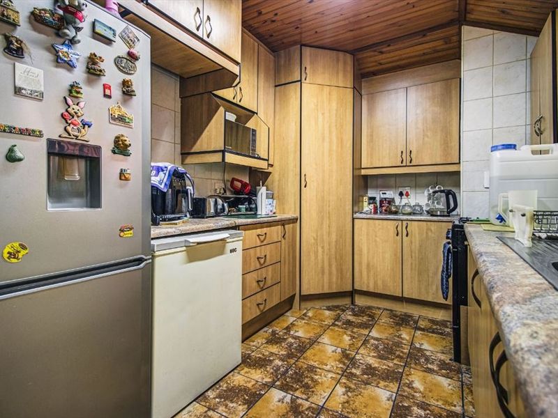 A compact kitchen featuring timber-look cabinetry, tiled flooring, and a timber-paneled ceiling, offering a functional layout with ample storage space.