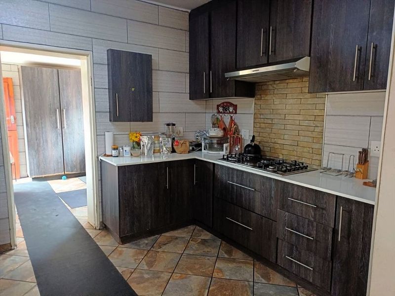 A functional kitchen featuring dark wood-look cabinetry, stone countertops, a gas hob with an extractor fan, and decorative tiled splashbacks.