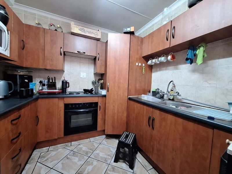 A functional kitchen featuring wood-look laminate cabinetry, built-in oven and hob, tiled backsplash, and durable tiled flooring.