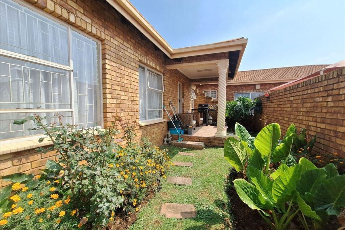 A rear view of the apartment featuring a face brick facade, a covered patio with a decorative column, and a private garden area.
