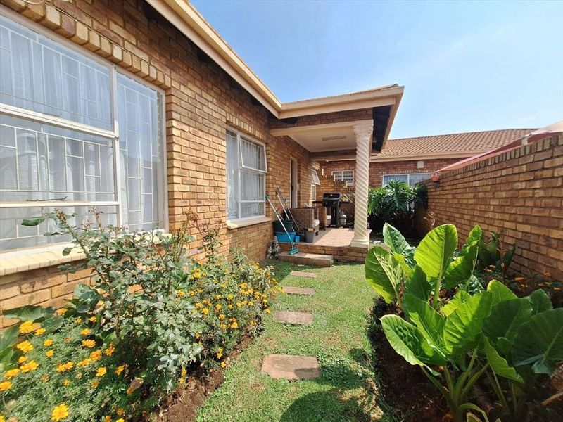 A rear view of the apartment featuring a face brick facade, a covered patio with a decorative column, and a private garden area.