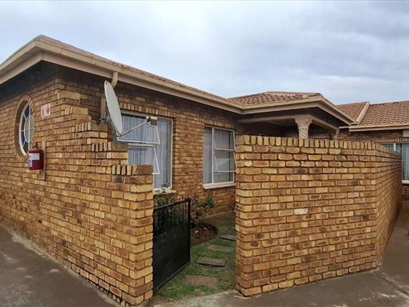 Front exterior view of a face brick townhouse featuring a paved driveway, covered carport, and established brick boundary walls.