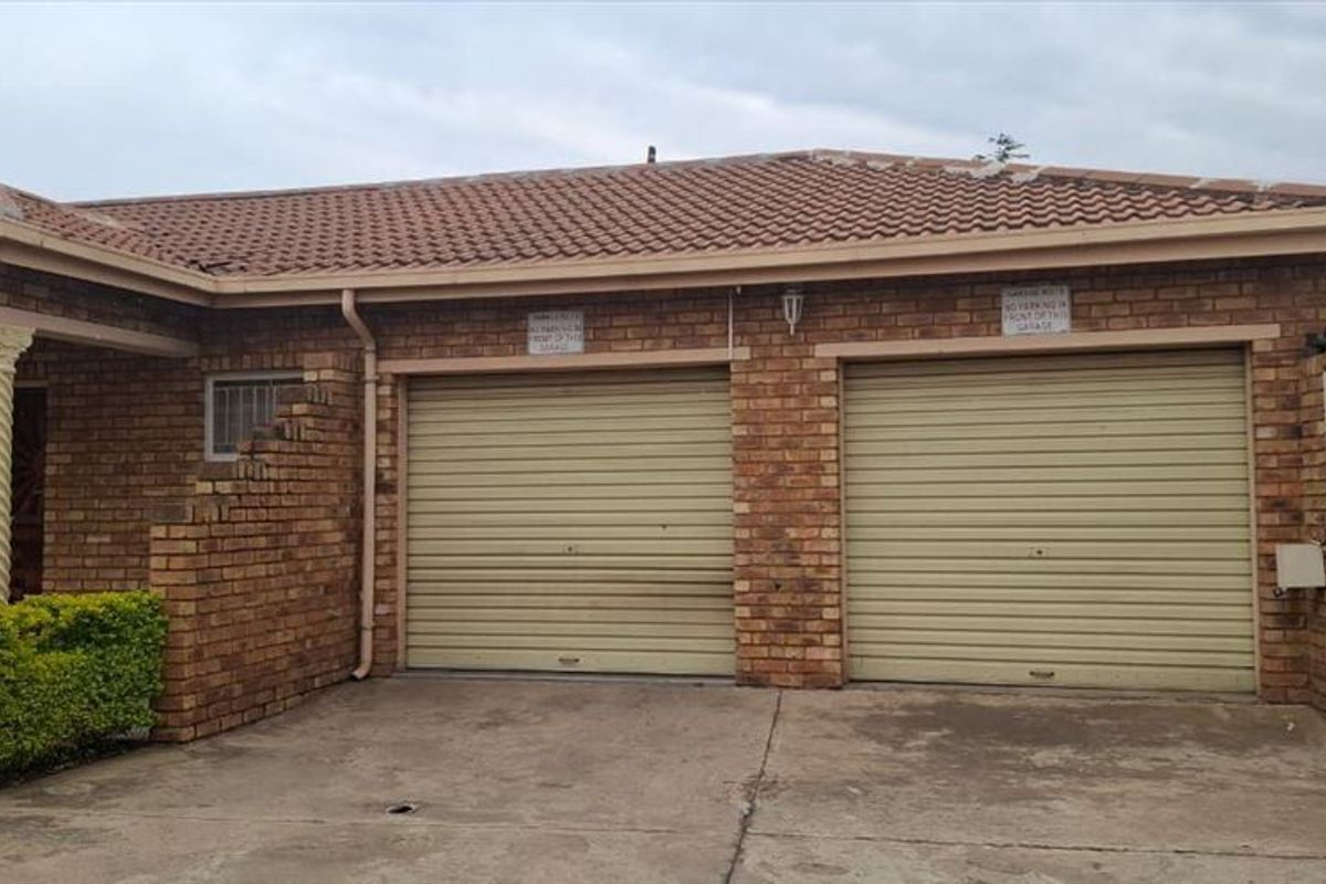 Front view of a townhouse featuring a double garage with roll-up doors, brick exterior, and a concrete driveway.