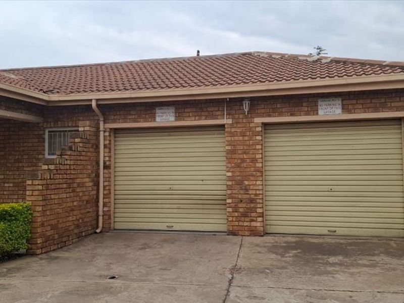 Front view of a townhouse featuring a double garage with roll-up doors, brick exterior, and a concrete driveway.