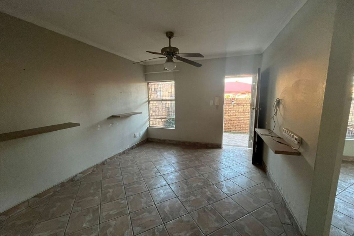 An empty living room featuring tiled flooring, a ceiling fan, and built-in wall shelving, with direct access to an outdoor area.