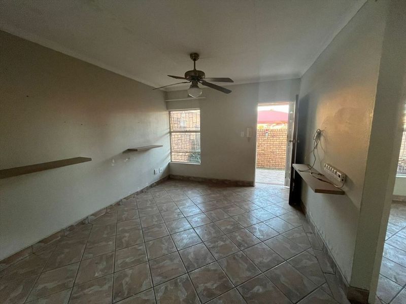 An empty living room featuring tiled flooring, a ceiling fan, and built-in wall shelving, with direct access to an outdoor area.