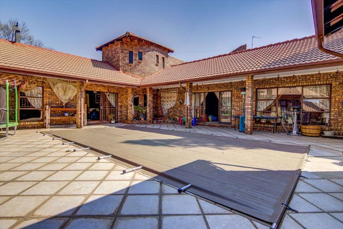 Spacious outdoor pool area featuring a covered patio, brick construction, and a large swimming pool with a protective cover.
