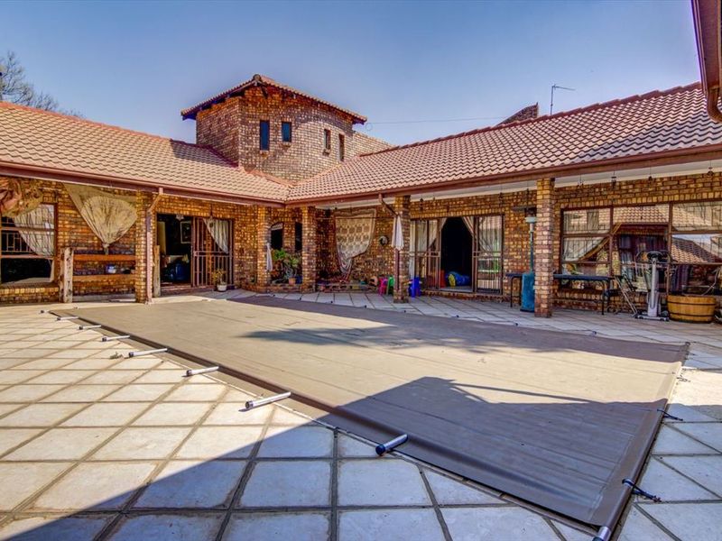 Spacious outdoor pool area featuring a covered patio, brick construction, and a large swimming pool with a protective cover.