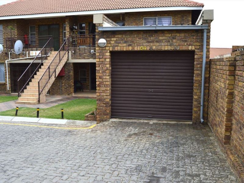 Front exterior view of a townhouse featuring a brick facade, a single roller garage door, and an external staircase leading to the upper level.