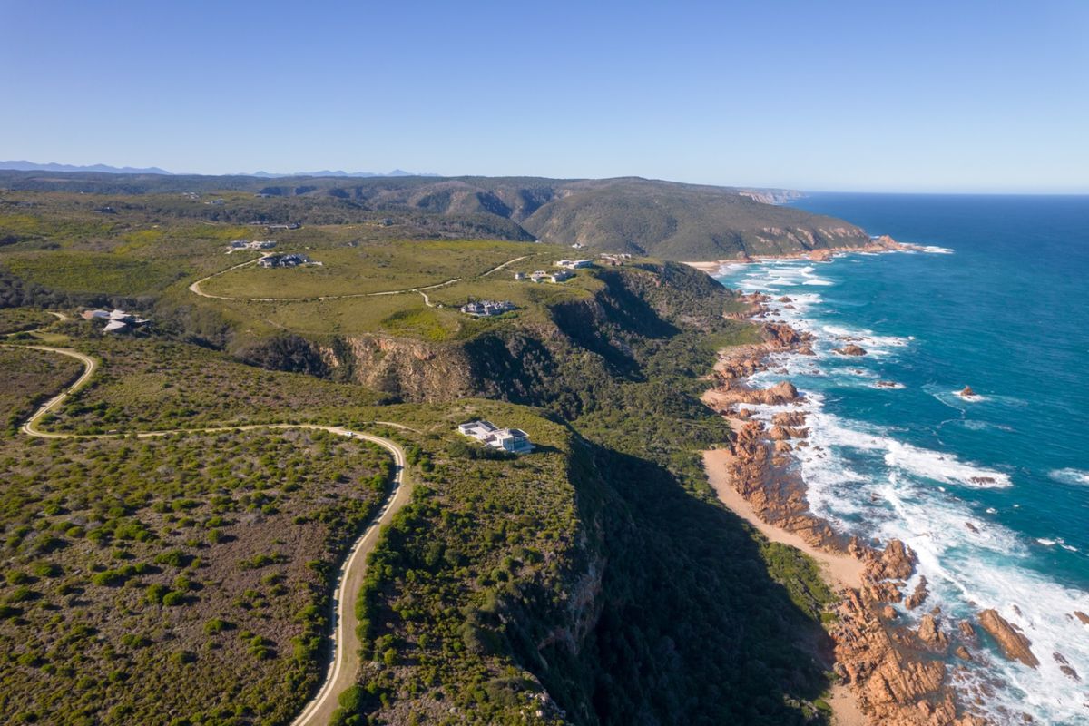 An aerial view of the coastal residential estate, showcasing the rugged coastline, natural vegetation, and winding access roads leading to the properties.
