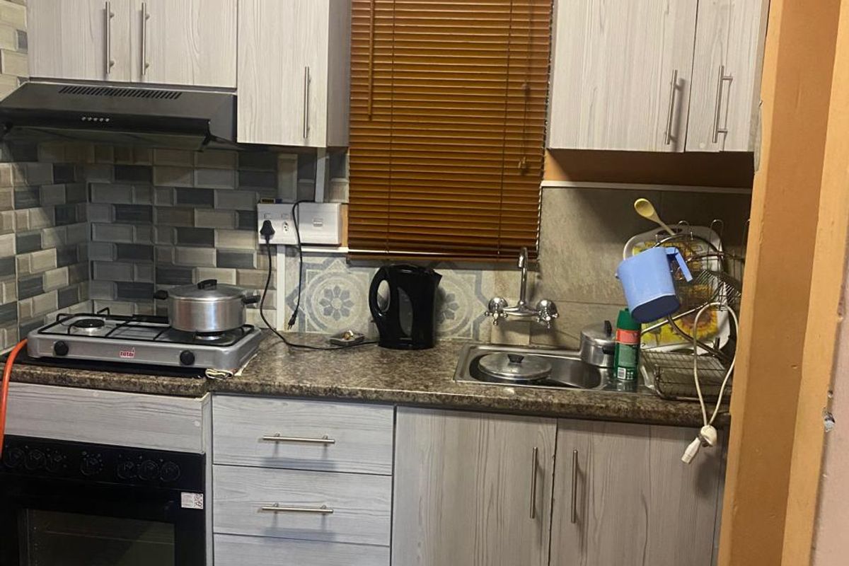 Compact kitchen featuring light wood-grain cabinetry, a gas hob with extractor fan, built-in oven, and a stainless steel sink with tiled backsplash.