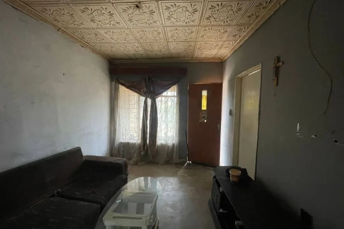 Living room featuring a unique decorative tin ceiling, solid entrance door, and security gate, requiring cosmetic updates to wall finishes and general maintenance.