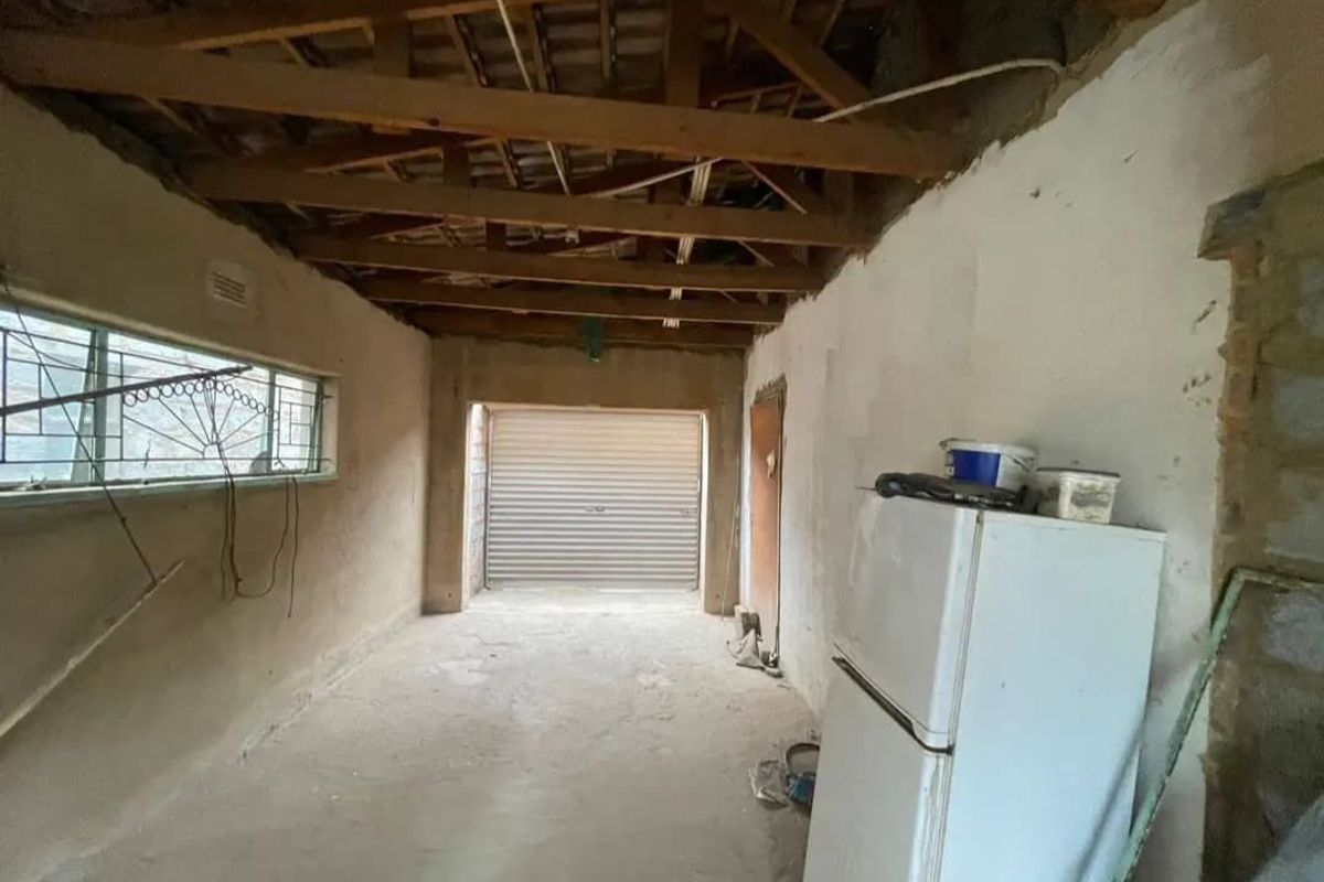 A raw, unfinished garage space featuring exposed timber roof trusses, concrete flooring, and a secure roller shutter door, offering significant potential for renovation.