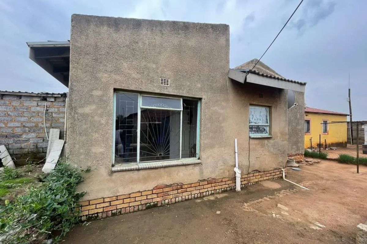 Rear view of a detached house featuring plastered masonry walls, metal window frames with security bars, and a brick plinth foundation.