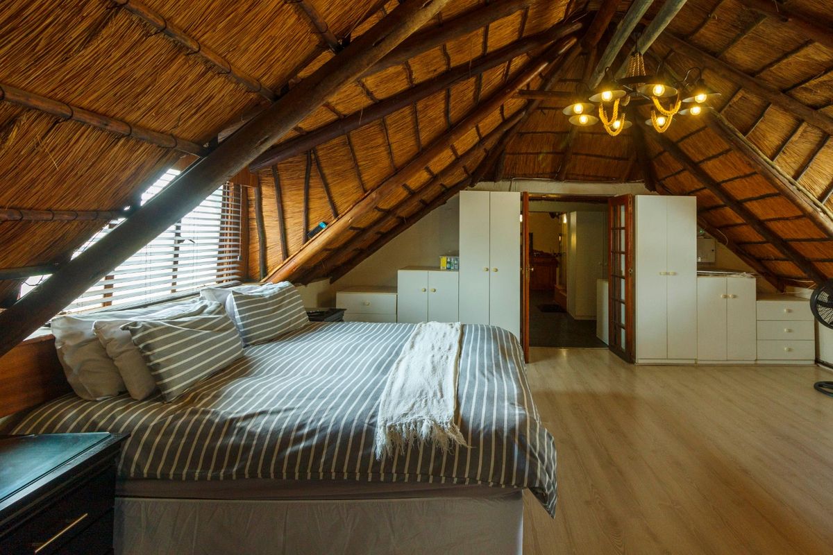 Spacious attic-style bedroom featuring a high vaulted thatched ceiling with exposed timber rafters, laminate flooring, and ample built-in cupboard storage.