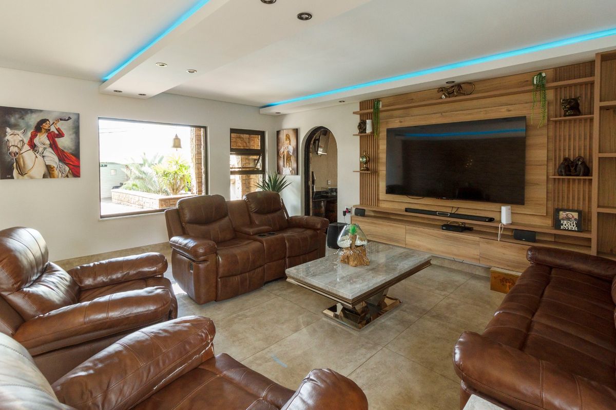 Spacious living room featuring a custom timber media wall, recessed ceiling with ambient LED lighting, and large format floor tiles.