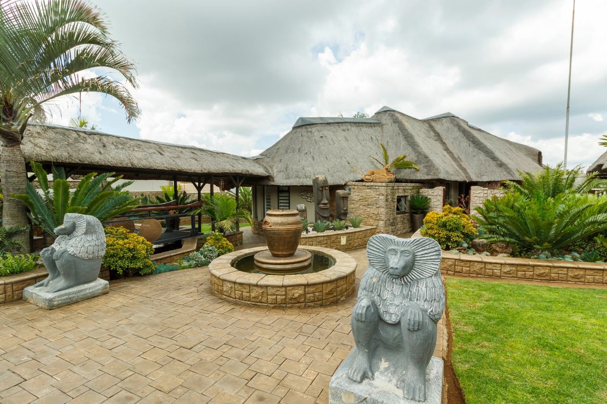 A well-maintained rear garden area featuring a thatched roof structure, stone-clad walls, a central water feature, and paved patio space.