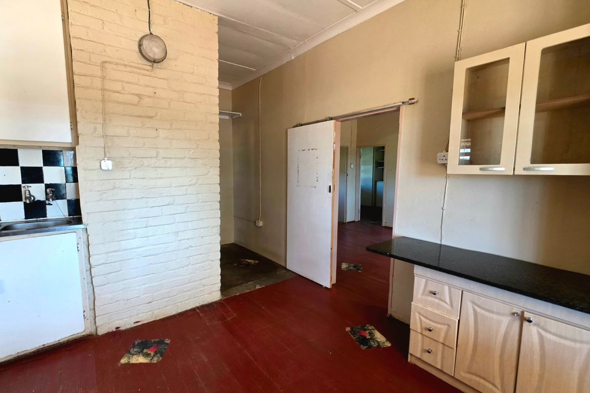 A dated kitchen area featuring exposed brickwork, built-in cabinetry, and a sink, offering significant potential for renovation and modernization.