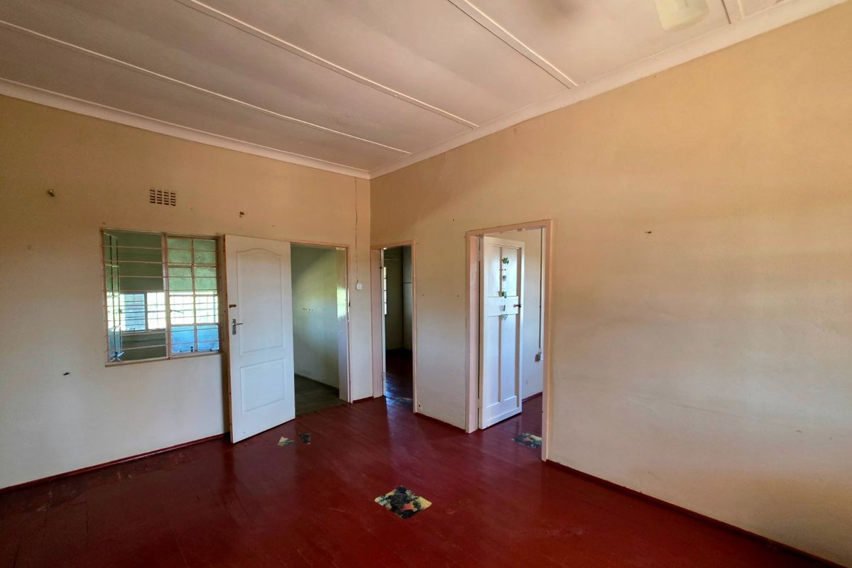An empty living room featuring original timber flooring, steel-framed windows, and multiple internal access points, offering a blank canvas for renovation.