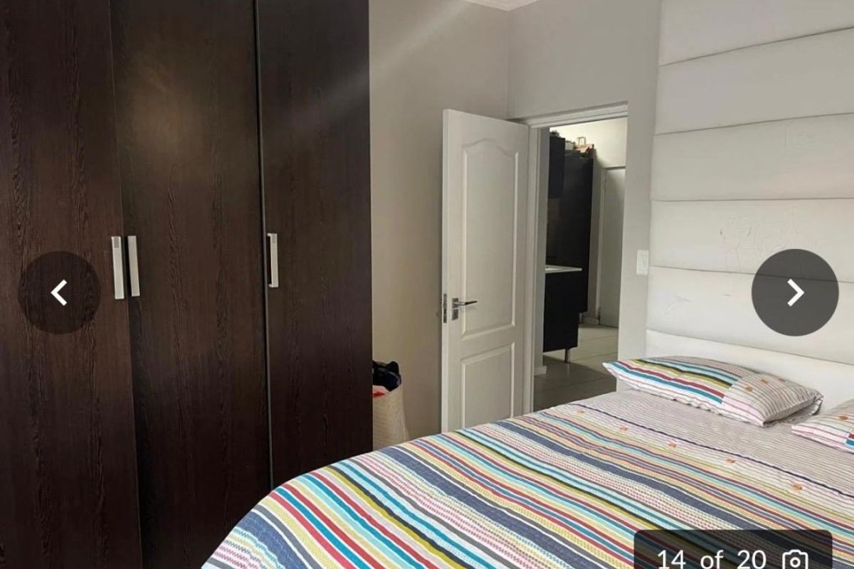 A bedroom featuring dark wood built-in cupboards and a large upholstered headboard, with a doorway leading to an adjacent room.