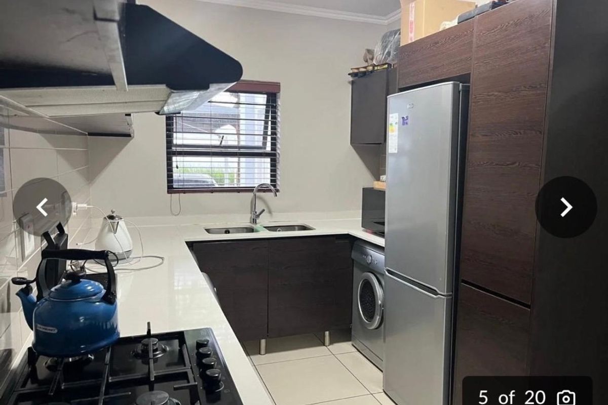 A functional kitchen featuring dark wood cabinetry, stone countertops, a gas hob with extractor fan, and integrated space for laundry appliances.