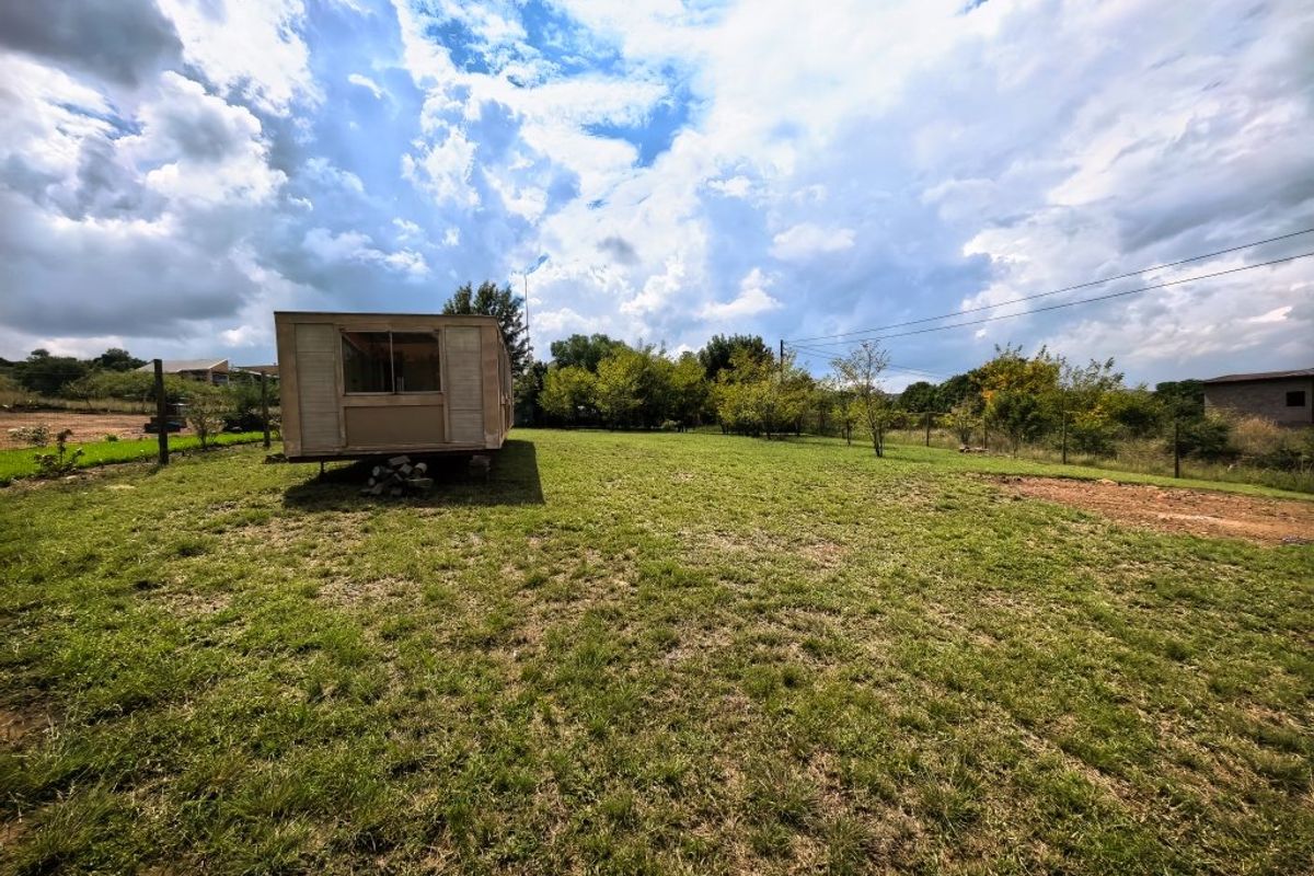 A wide-angle view of a residential vacant land plot featuring a grassy lawn, perimeter fencing, and an existing mobile structure.