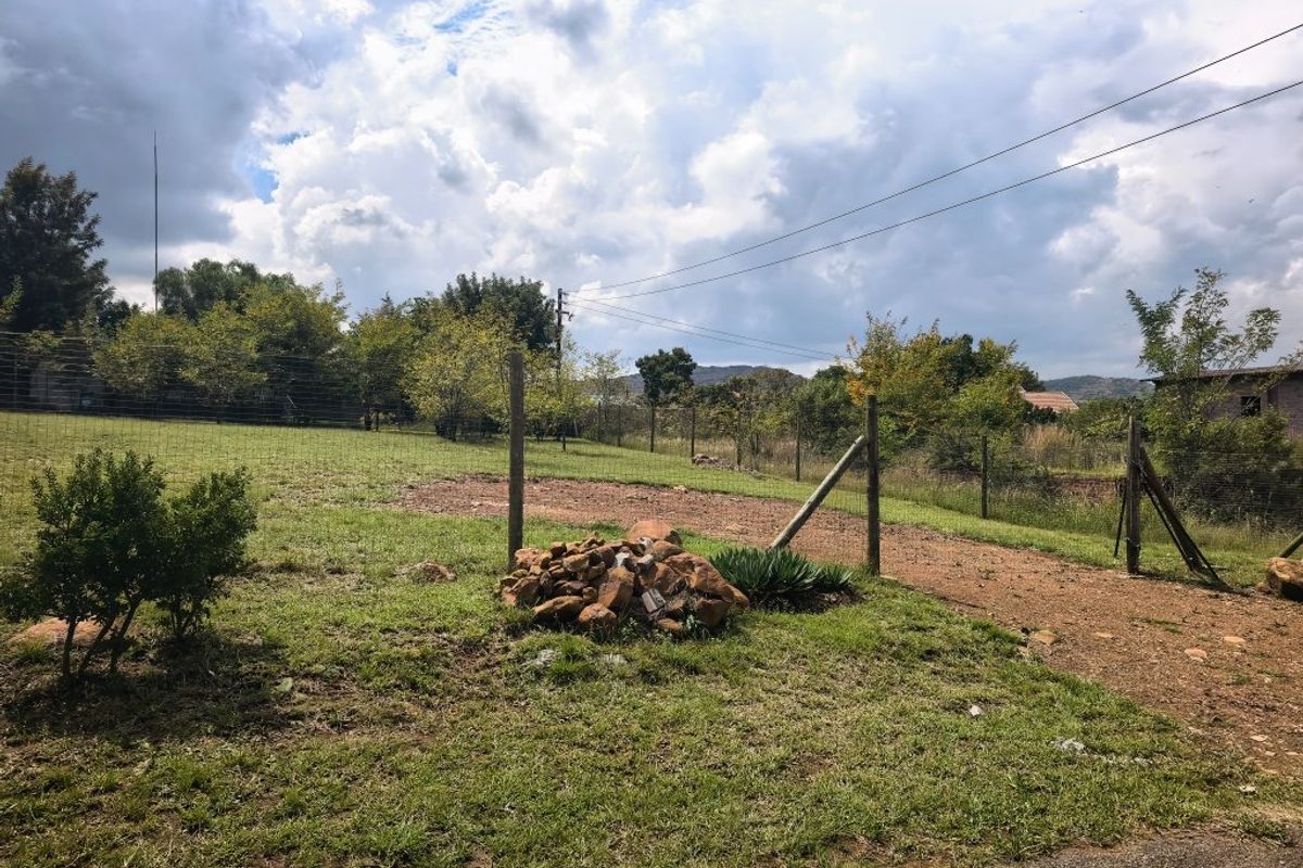 A view of the vacant residential land featuring grassy terrain, wire perimeter fencing, and established trees under a cloudy sky.