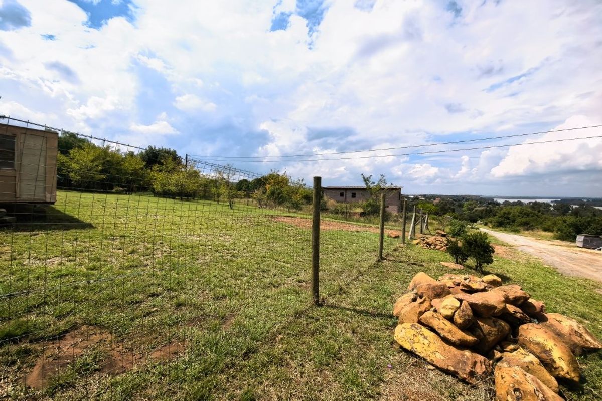 A view of a residential plot featuring wire mesh fencing, wooden posts, and natural rock formations with a distant landscape view.