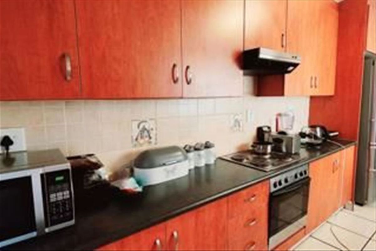 A functional kitchen featuring wood-finish cabinetry, dark countertops, a tiled backsplash, and integrated cooking appliances including an oven, hob, and extractor fan.