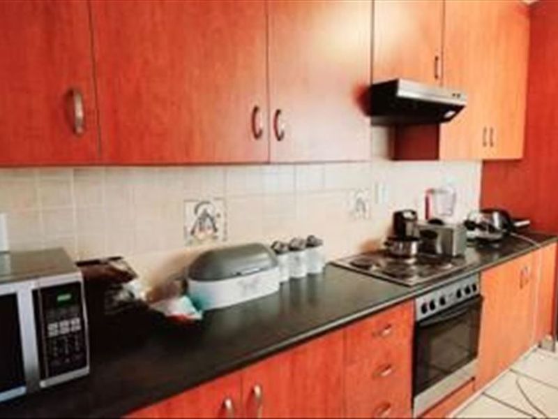 A functional kitchen featuring wood-finish cabinetry, dark countertops, a tiled backsplash, and integrated cooking appliances including an oven, hob, and extractor fan.