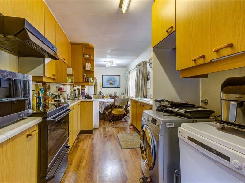 A functional galley-style kitchen featuring wood-look cabinetry, integrated appliances, and laminate flooring, leading into an adjacent dining area.