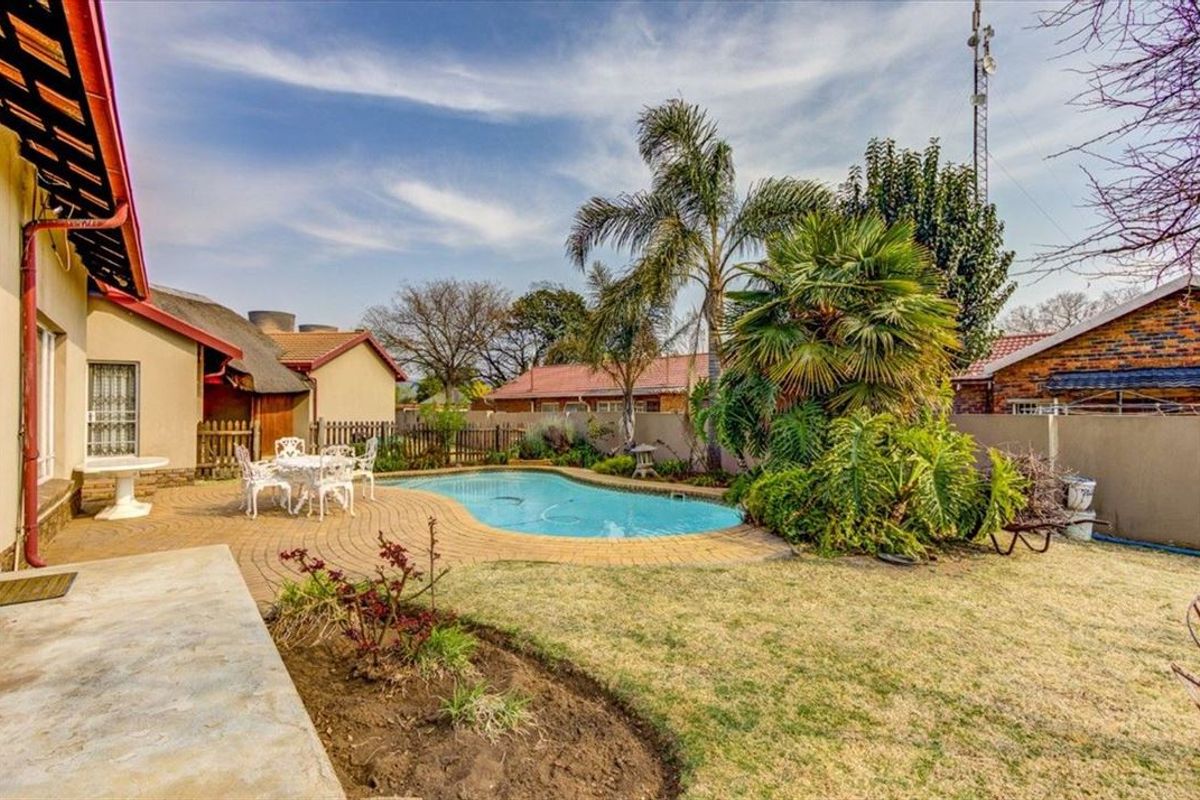 A backyard area featuring a swimming pool, paved patio space, and established garden landscaping, adjacent to the main house structure.