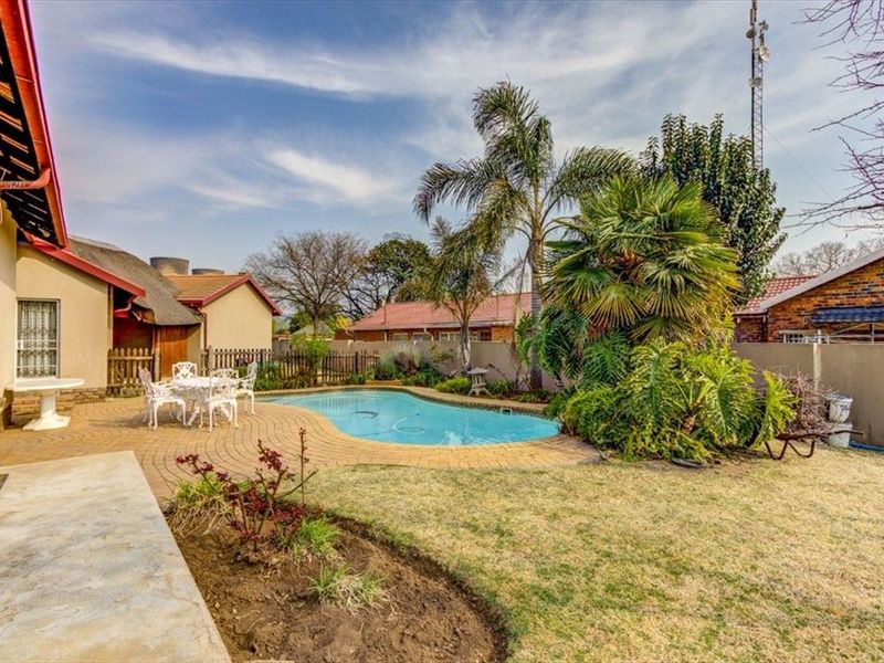 A backyard area featuring a swimming pool, paved patio space, and established garden landscaping, adjacent to the main house structure.