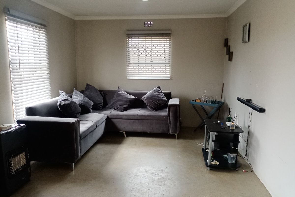 A living room featuring concrete flooring, neutral walls, and venetian blinds, offering a functional space with potential for modern updates.