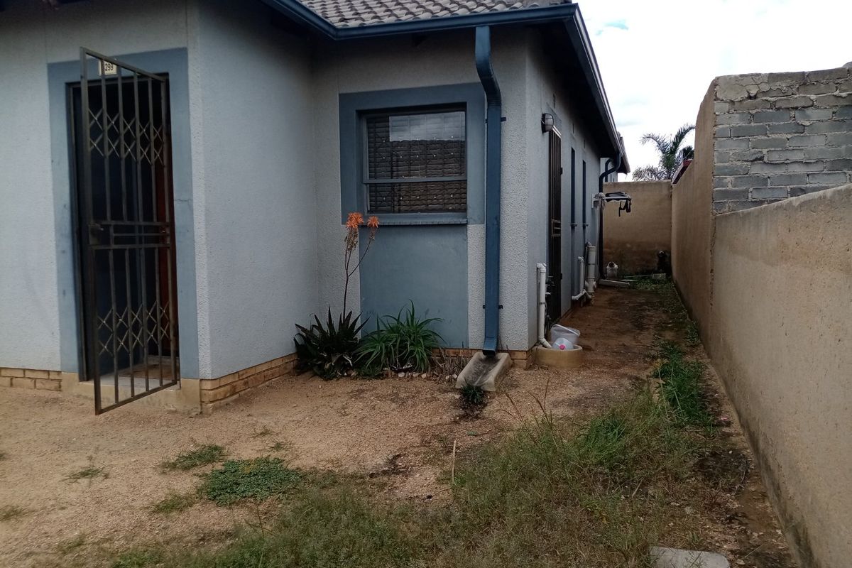 Rear exterior view of the house featuring a security gate, tiled roof, and a side yard area with boundary walling.