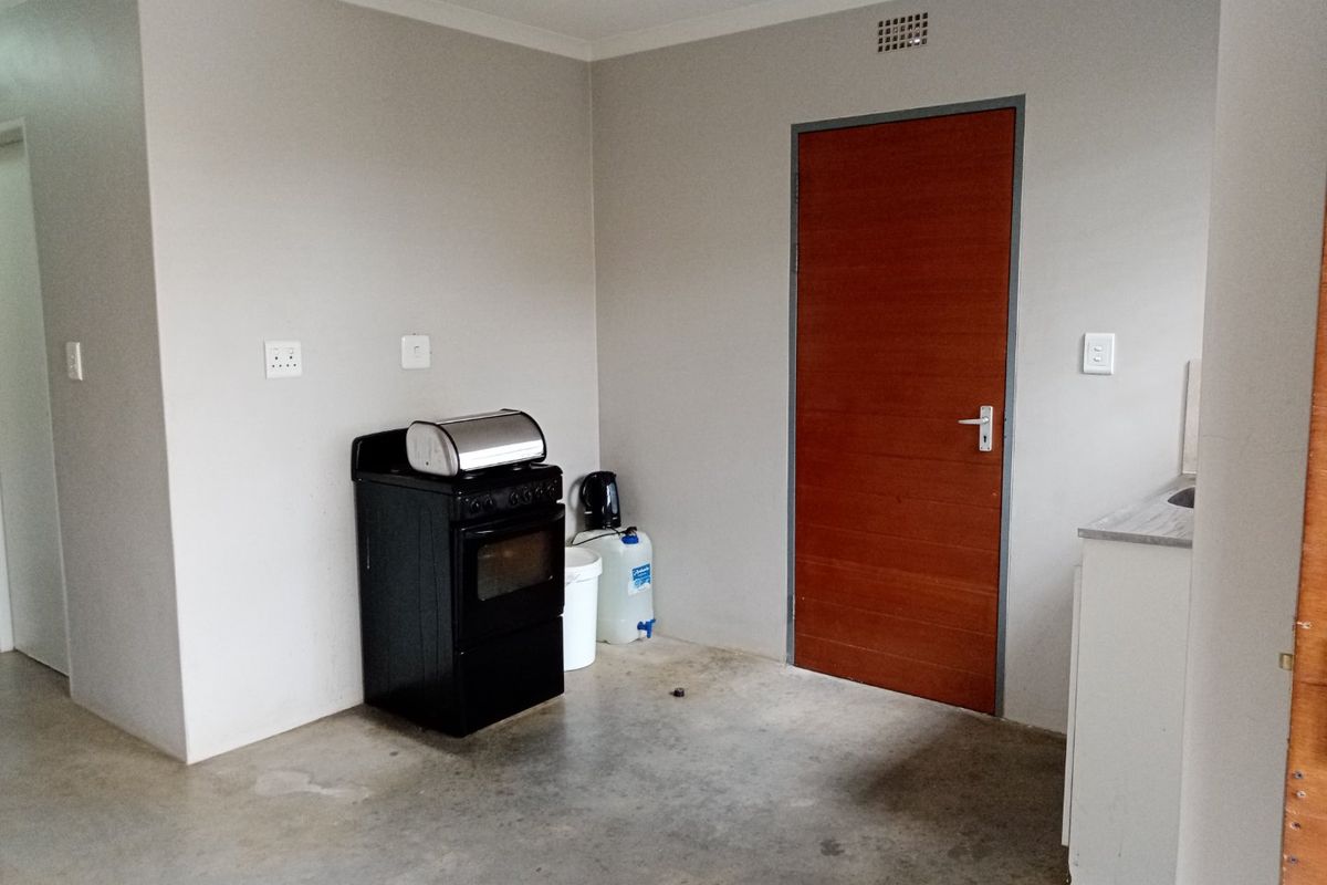 A basic kitchen area featuring a freestanding stove, simple cabinetry, and unfinished concrete flooring, offering a blank canvas for potential renovation.