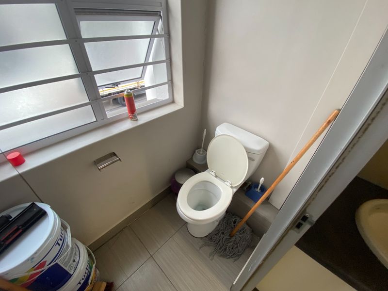 A compact commercial restroom featuring a standard toilet, tiled flooring, and a window with security bars.