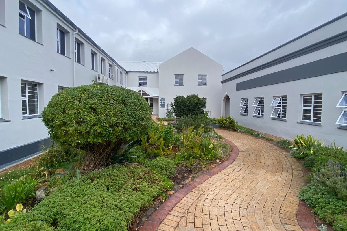 A well-maintained commercial courtyard featuring a curved brick pathway, landscaped garden beds, and surrounding multi-story office building facades with white painted finishes.