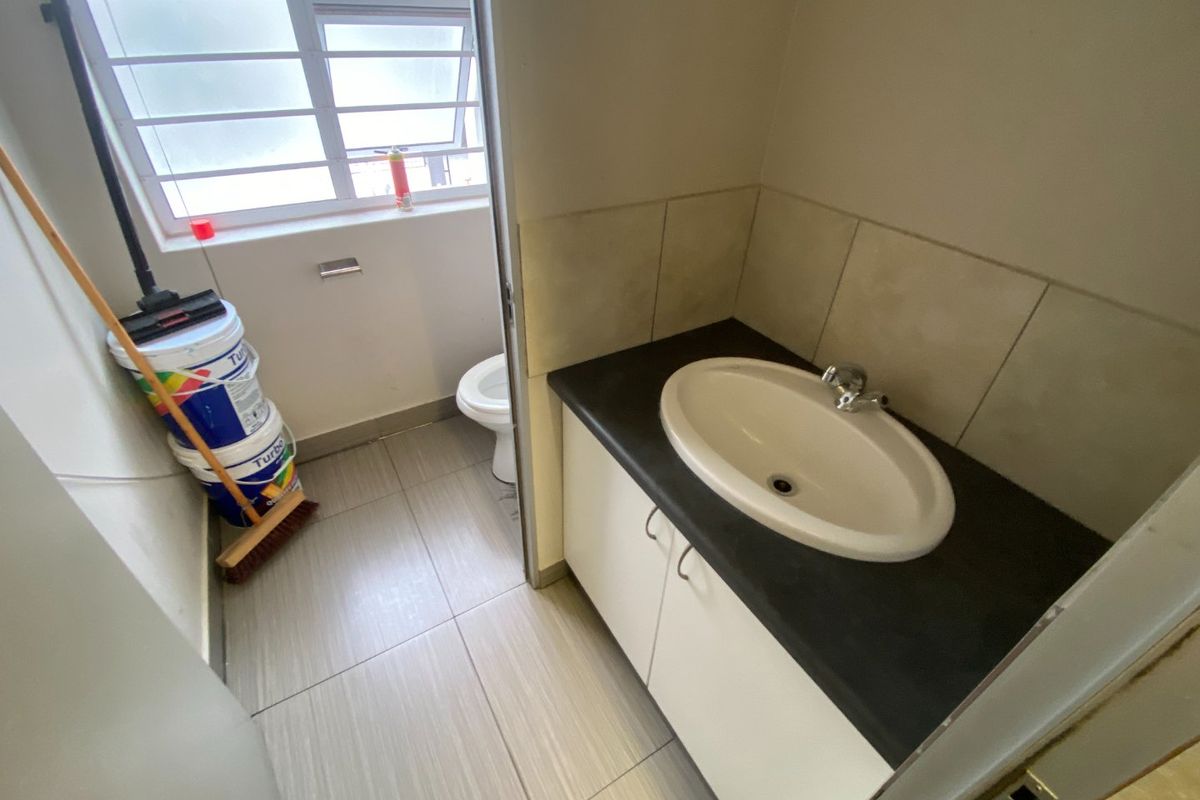 A functional commercial restroom featuring a vanity with a drop-in basin, tiled flooring, and a separate toilet area with a window.