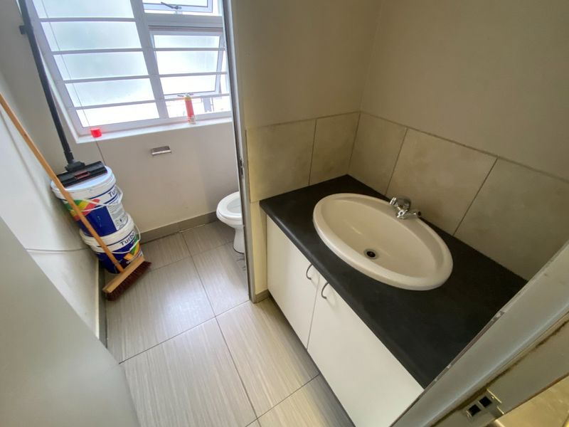A functional commercial restroom featuring a vanity with a drop-in basin, tiled flooring, and a separate toilet area with a window.