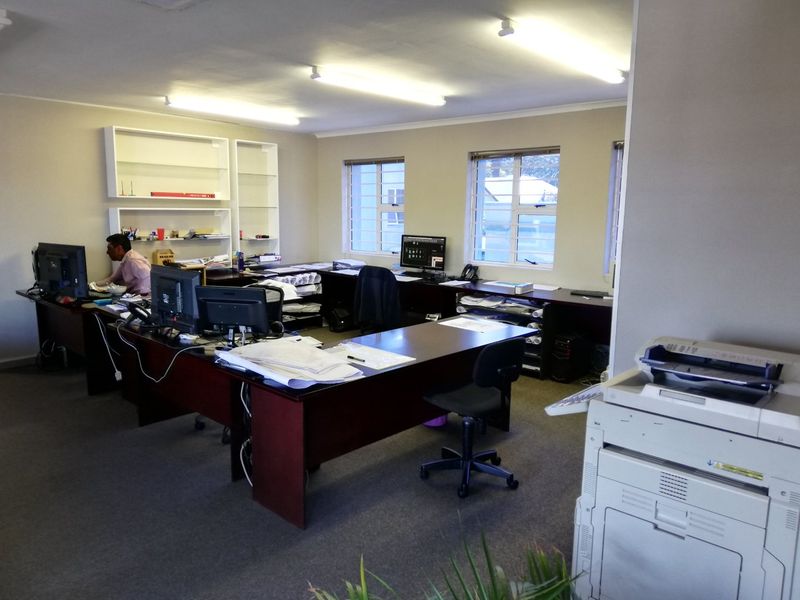 A functional commercial office space featuring built-in shelving, large windows with security bars, and overhead fluorescent lighting.