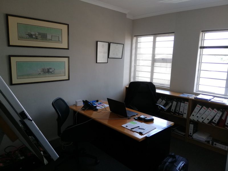 A functional commercial office space featuring built-in shelving units, large windows with horizontal blinds, and neutral wall finishes.