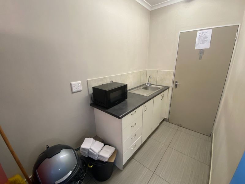 A compact kitchenette area featuring built-in cabinetry, a stainless steel sink, tiled splashback, and tiled flooring.