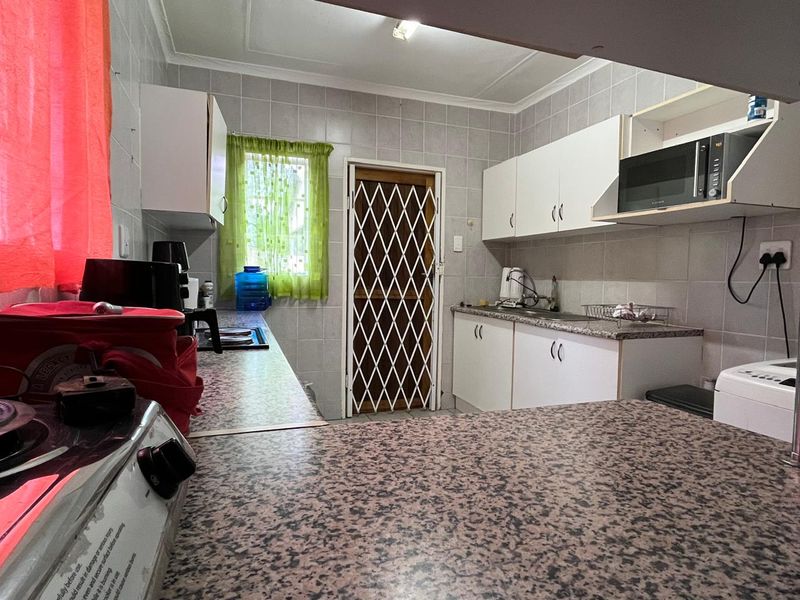 A functional kitchen featuring laminate countertops, tiled wall finishes, built-in cabinetry, and a secure exterior door with a metal security gate.
