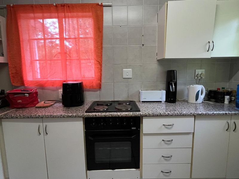 A functional kitchen featuring built-in cabinetry, a tiled backsplash, and a standard electric oven and hob setup.