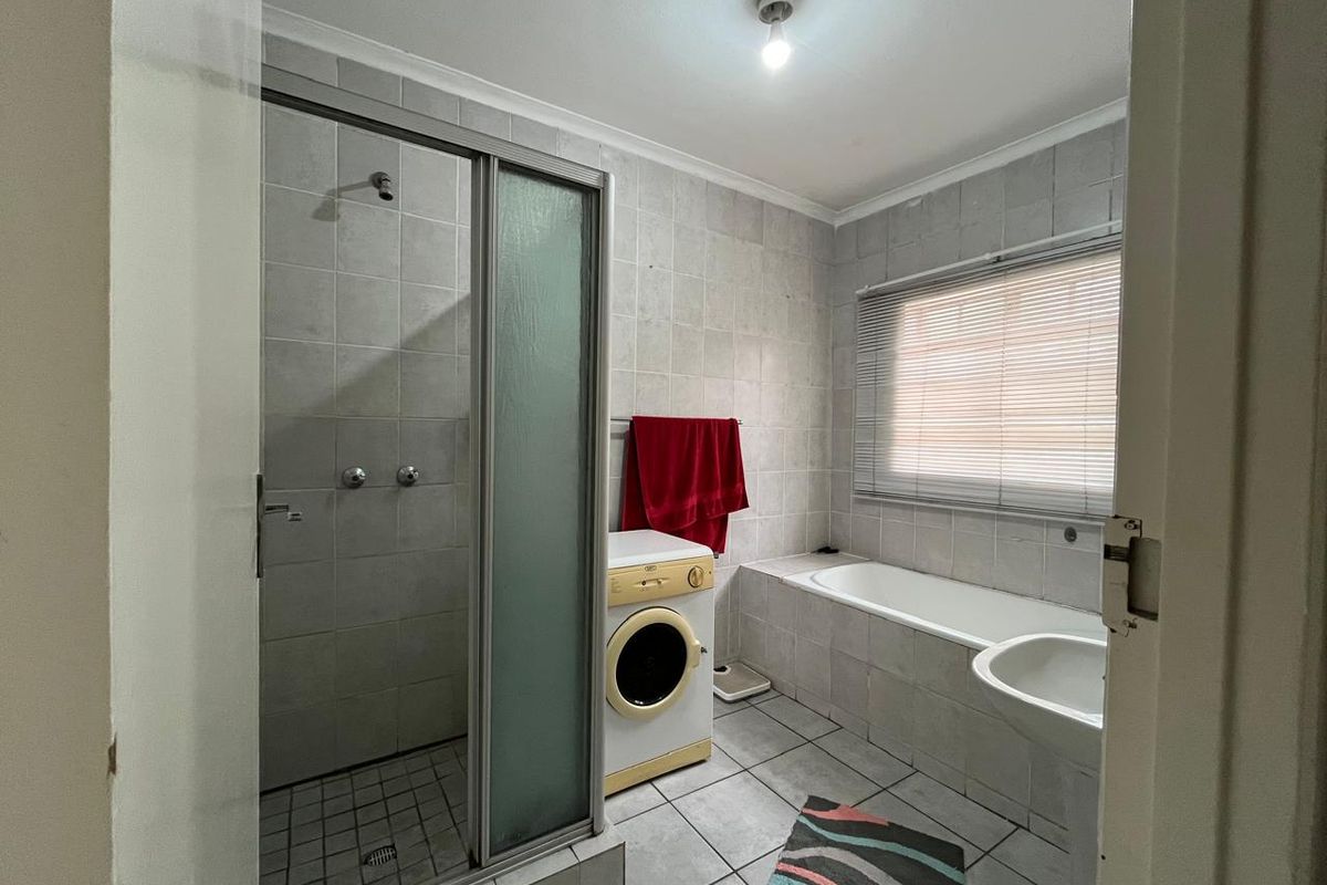 A functional bathroom featuring a shower enclosure, bathtub, and pedestal basin with neutral wall and floor tiling.
